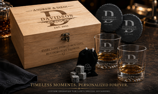 Personalized whiskey gift set including a wooden box engraved with 'ANDREW & SARAH DAVIDSON', two engraved rocks glasses, two slate coasters, and a small black drawstring pouch on a dark wooden table.