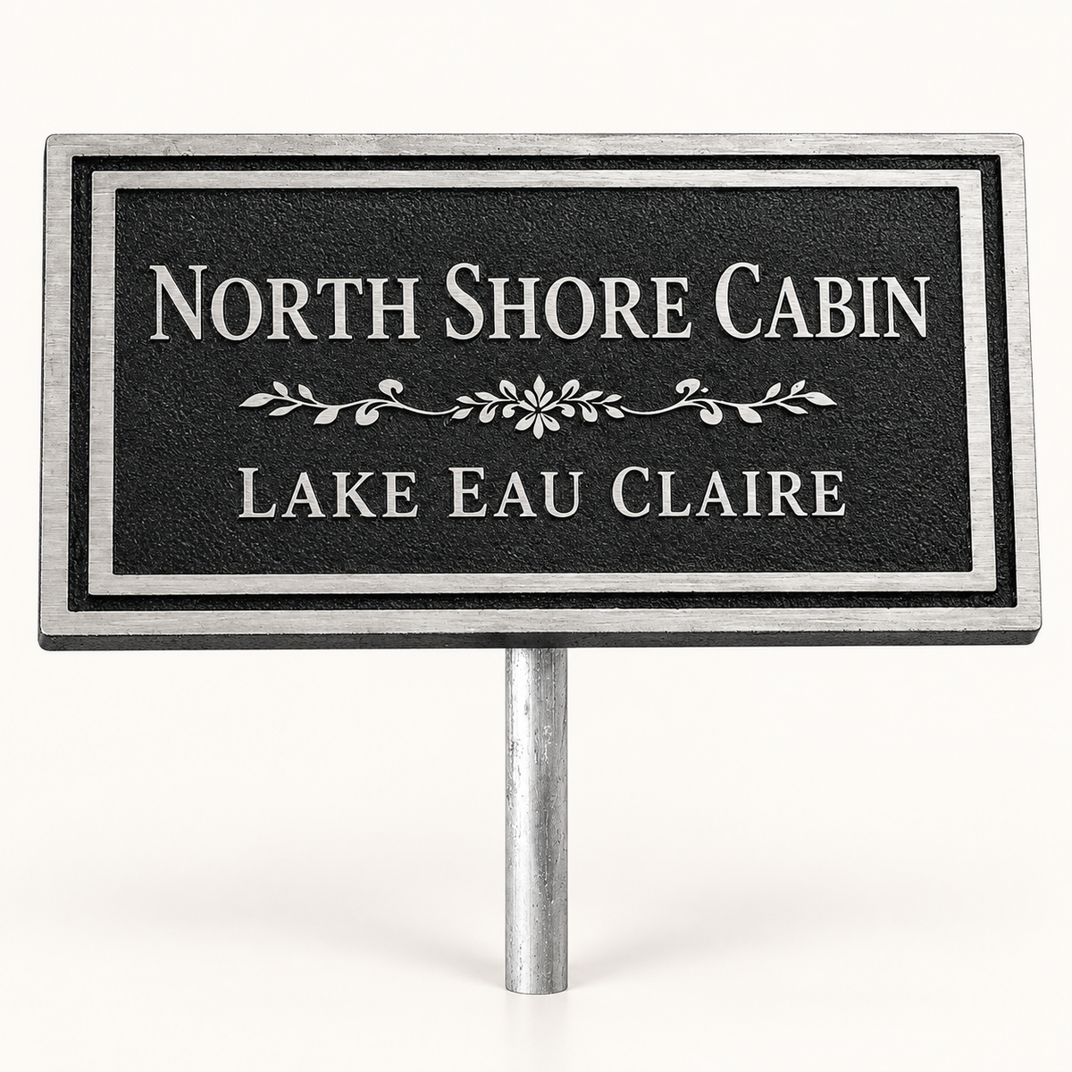 A rectangular black sign with silver border and silver text reading 'NORTH SHORE CABIN' and 'LAKE EAU CLAIRE', mounted on a silver metal stake against a plain white background.