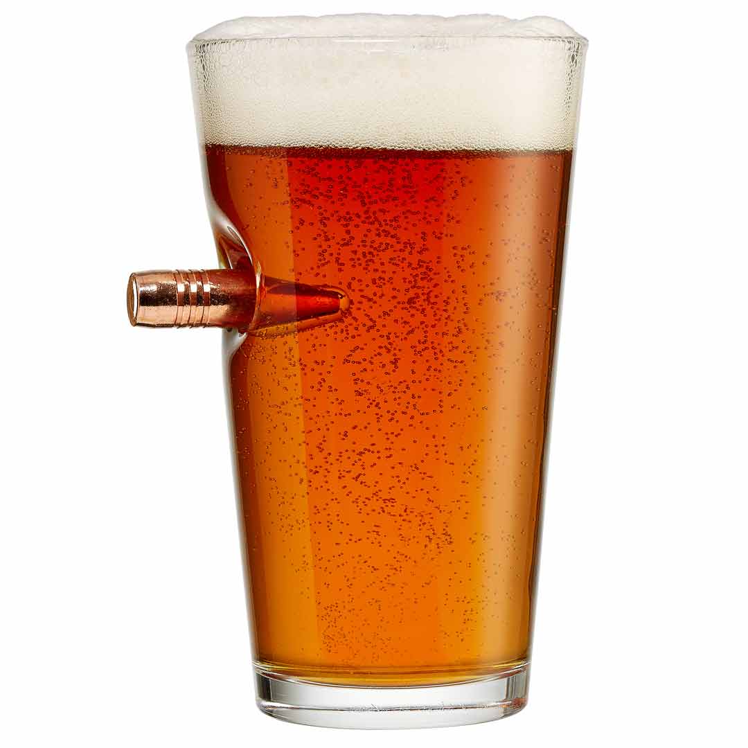 Pint glass with a bullet embedment filled with beer on a white background