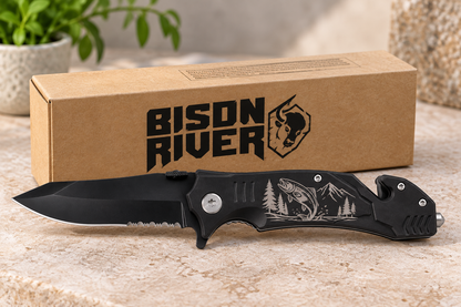A black folding pocket knife with a fish and mountain engraving on the handle, displayed in front of its brown cardboard packaging box printed with the Bison River logo.