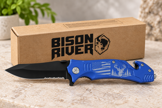 A blue and black folding pocket knife with a black blade and a blue handle featuring a deer and American flag engraving, displayed in front of its brown cardboard packaging box with the 'Bison River' logo.