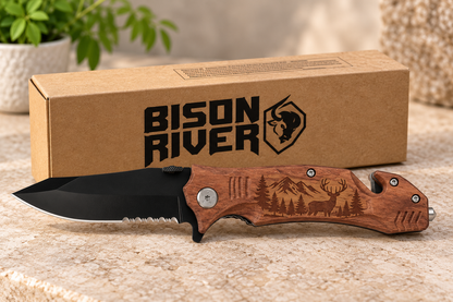A folding pocket knife with a black blade and a brown engraved wooden handle lies in front of its brown cardboard packaging box. The box features the 'Bison River' brand logo.