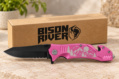 A pink folding pocket knife with a black blade and silver mountain engraving, displayed in front of its brown cardboard packaging box with the 'Bison River' logo.