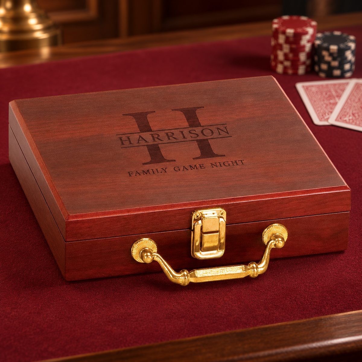 A personalized reddish-brown wooden poker case with a gold handle and latch, engraved with 'HARRISON' and 'FAMILY GAME NIGHT' on the lid, displayed on a red felt surface with cards and poker chips in the background.