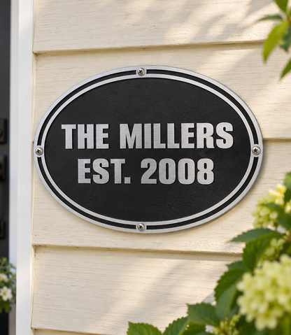 Personalized black oval cast aluminum Millers sign mounted on light exterior siding