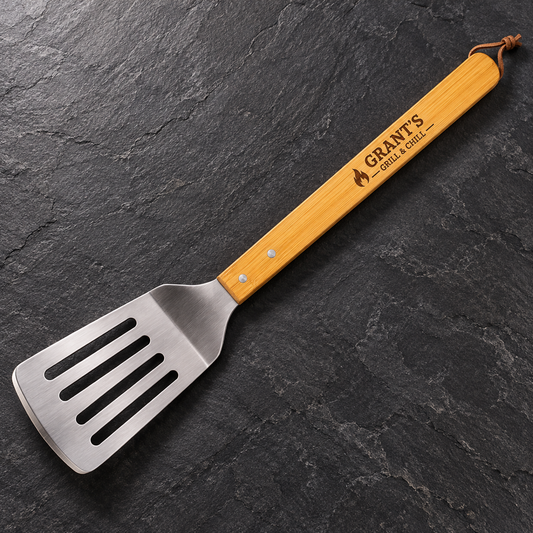 Bamboo barbecue spatula engraved Grant’s Grill & Chill on a dark slate surface