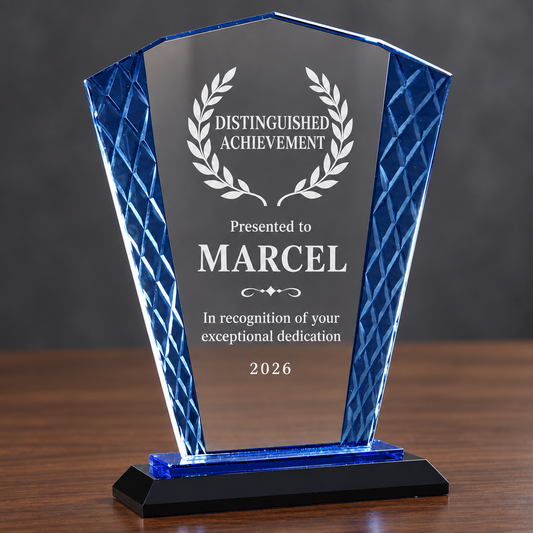 A personalized acrylic award plaque on a black base, featuring a clear central panel engraved with 'Distinguished Achievement' and the name 'MARCEL', flanked by textured blue side panels, set on a wooden surface against a dark gray background.