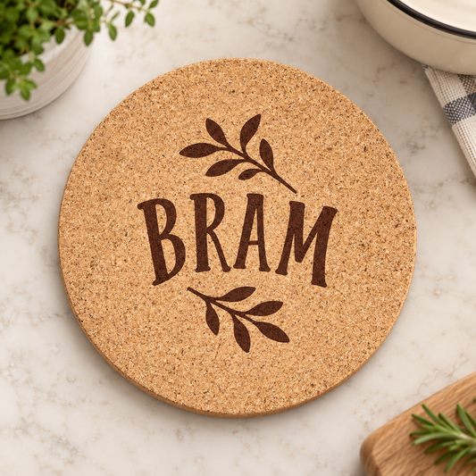 Round cork trivet engraved BRAM with leafy accents on a kitchen surface.