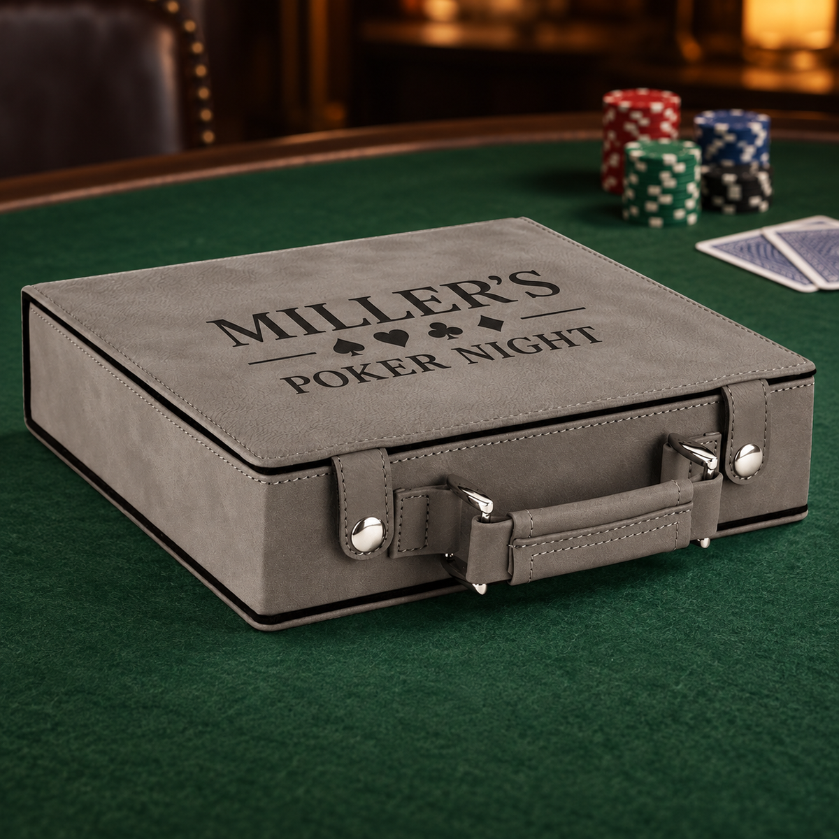 A gray faux-leather poker case with 'MILLER'S POKER NIGHT' printed on the lid, placed on a green felt poker table with poker chips and cards nearby.