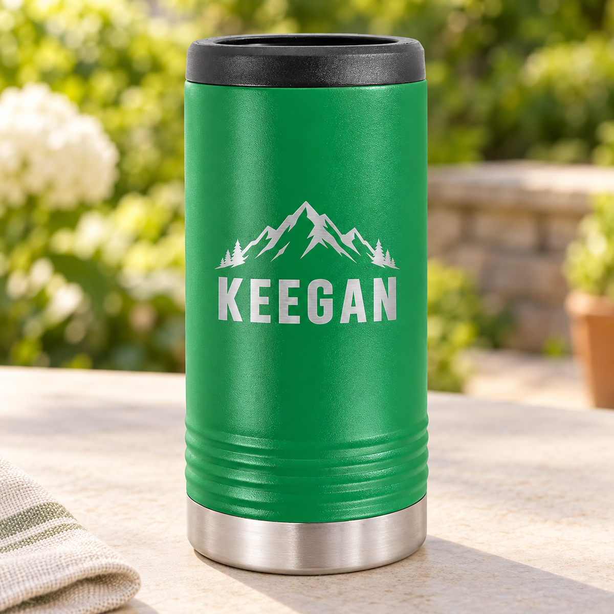 Green slim can cooler with silver KEEGAN mountain engraving and black top rim.