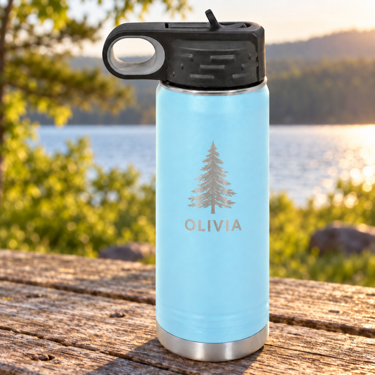 Light-blue 20 oz water bottle with OLIVIA and an evergreen tree engraved in silver, a black straw lid and silver base, beside a lake.