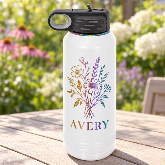 White 32 oz ion-plated water bottle with rainbow AVERY / wildflower engraving with a black straw lid, on a garden patio table.