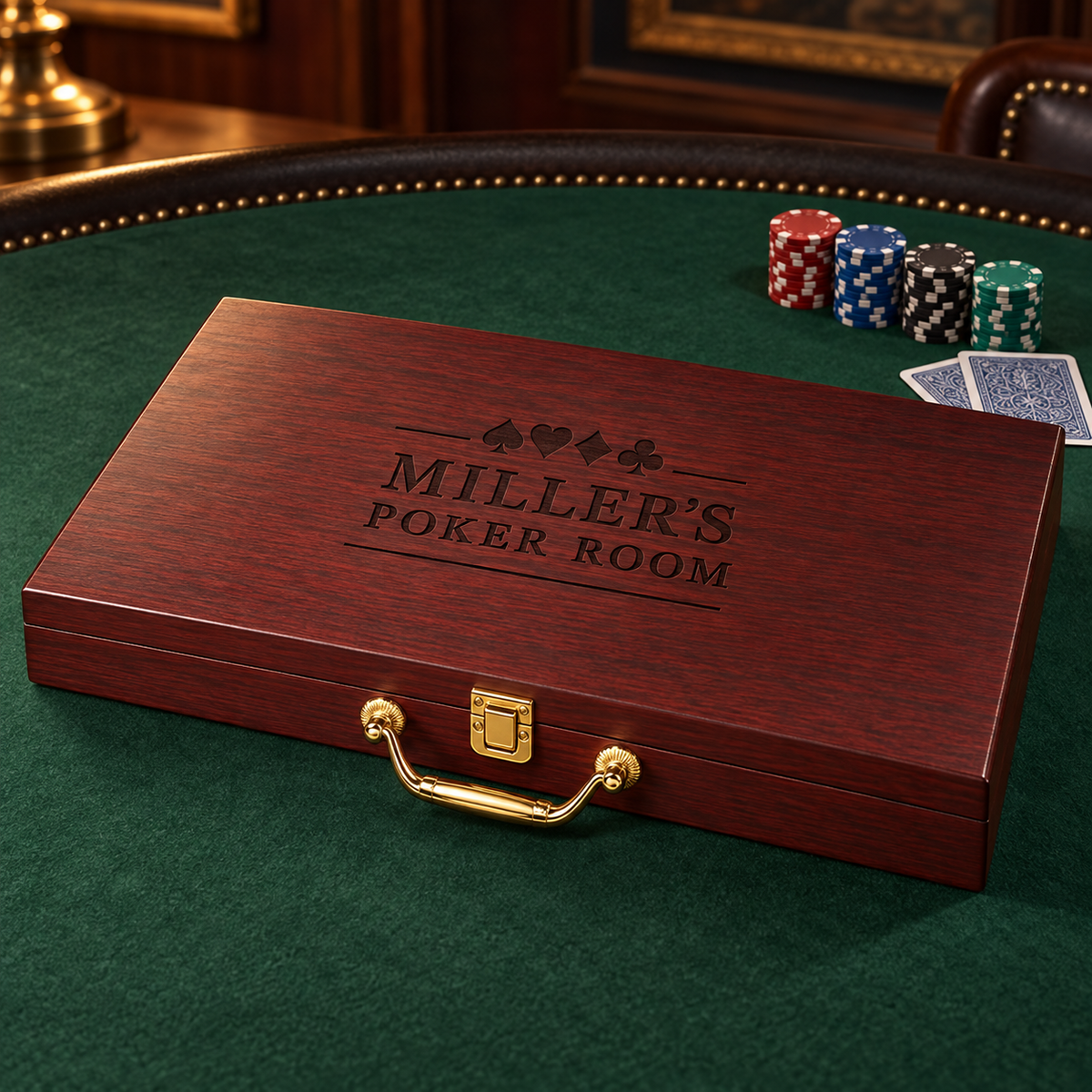 A polished reddish-brown wooden poker box with a gold handle and clasp, engraved with 'MILLER'S POKER ROOM' and four card suits, placed on a green felt poker table with chips and cards nearby.