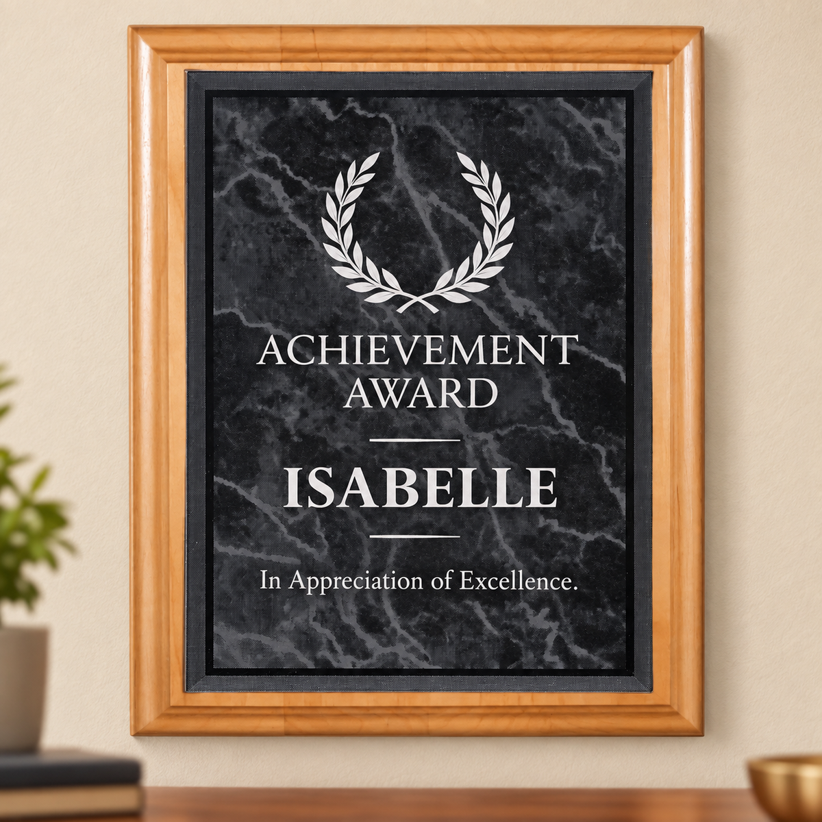 A framed personalized achievement award plaque featuring a black marble faceplate with white text reading 'ACHIEVEMENT AWARD ISABELLE In Appreciation of Excellence' and a white laurel wreath, shown on a red alder plaque against a beige wall.