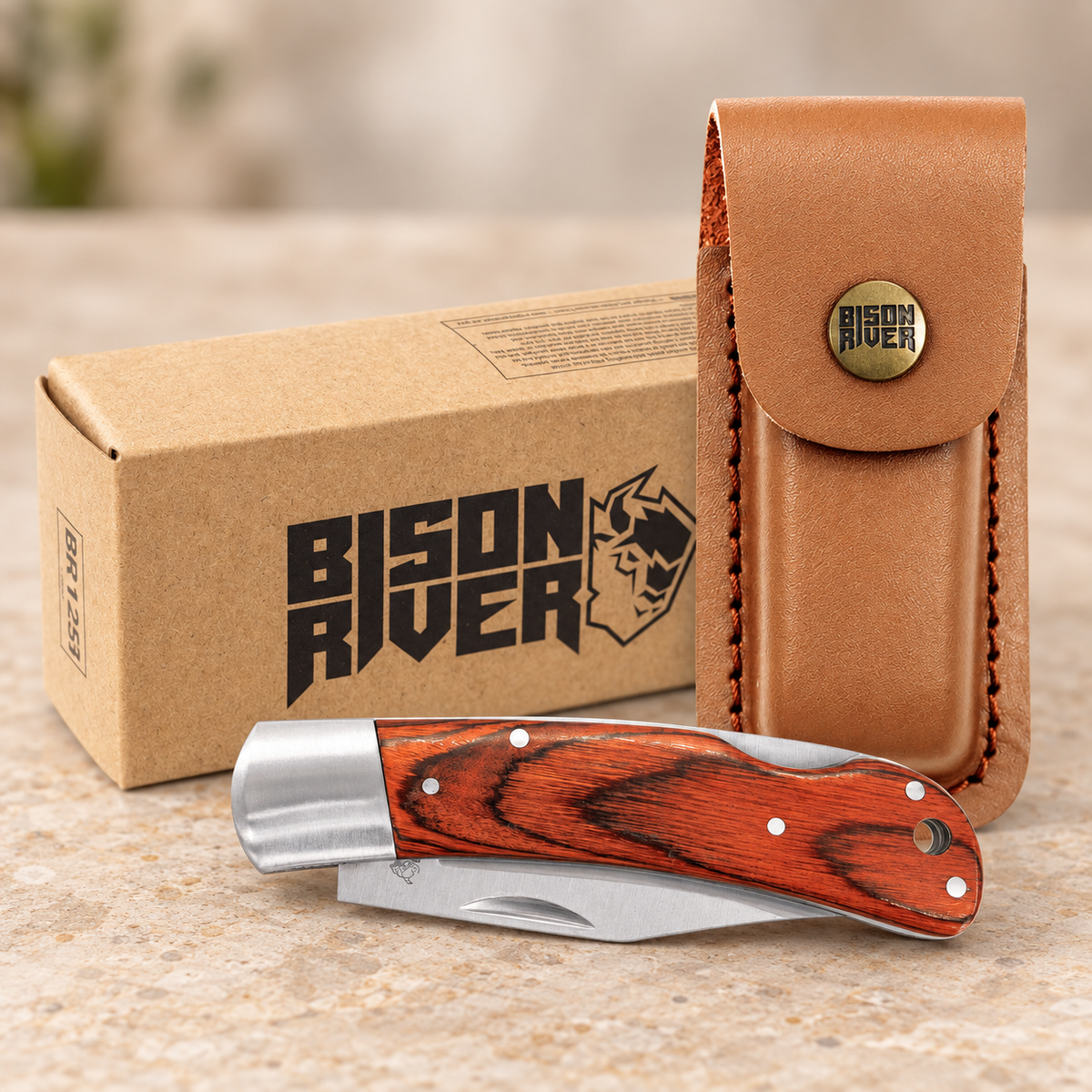 A folding pocket knife with a reddish-brown wood handle and silver steel blade, displayed in front of its brown cardboard box and a tan leather pouch. The box and pouch feature the 'Bison River' brand logo.